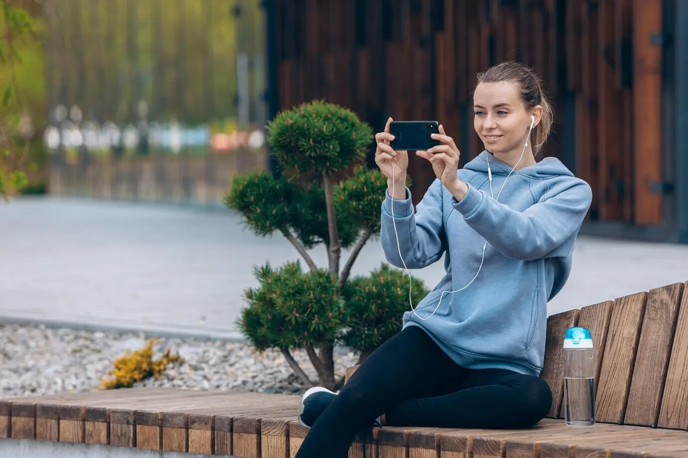 Ein Mädchen sitzt auf einer Bank auf ihrem Bein und macht ein Selfie.